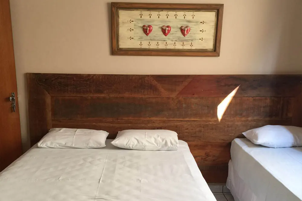 Quarto com cama de casal e cama de solteiro, cabeceira de madeira rústica